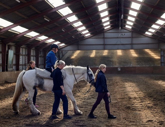 Patient med hjerneskade fra Center for Neurorehabilitering rider på hest, mens hjælpere støtter og trækker